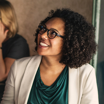 a woman with dark curly hair and glasses looks up at an unseen person