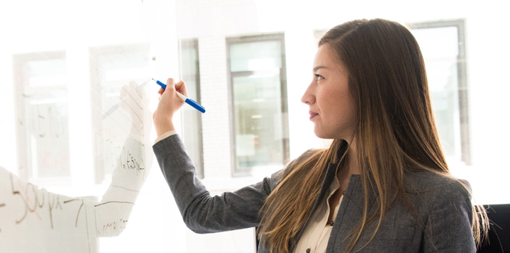 a woman in a blazer writes on a whiteboard