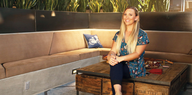 a woman with long blonde hair sits outside in an outdoor living room