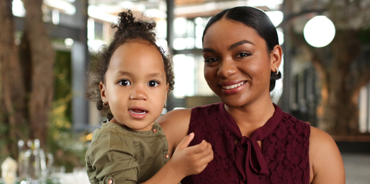 A woman with her hair in a bun and sleeveless top holds her toddler 