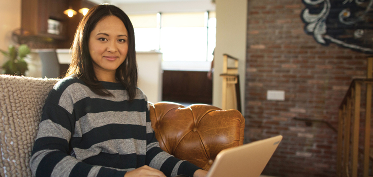 woman sits on her couch with a laptop in her lap