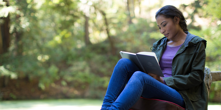 a woman sits outside reading a book in her lap