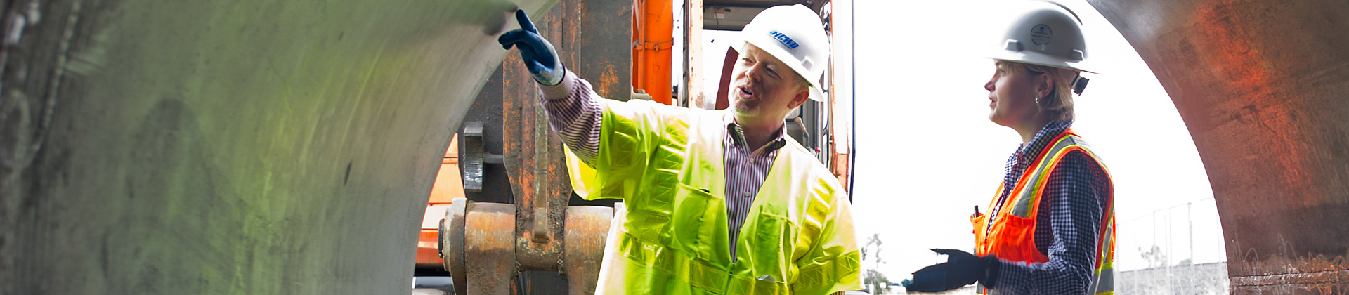  Two people in hardhats and safety vests look at a giant pipe