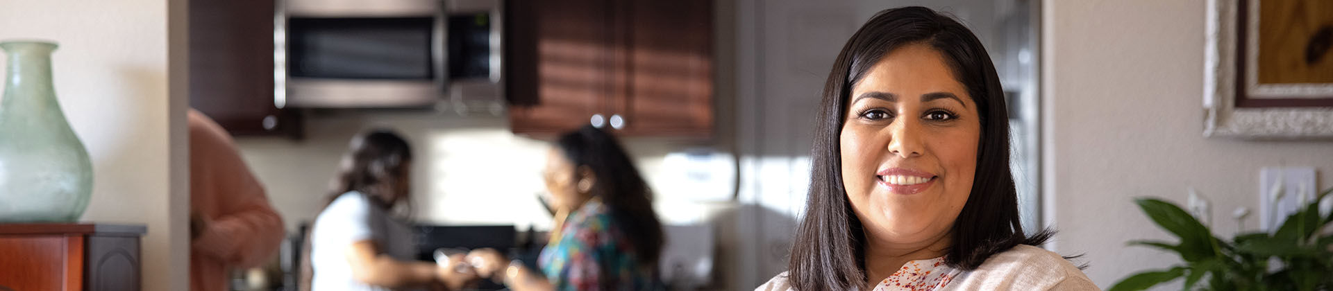 Closeup of Elizabeth V., Class of 2023, standing in a kitchen. There are two other women in the background talking