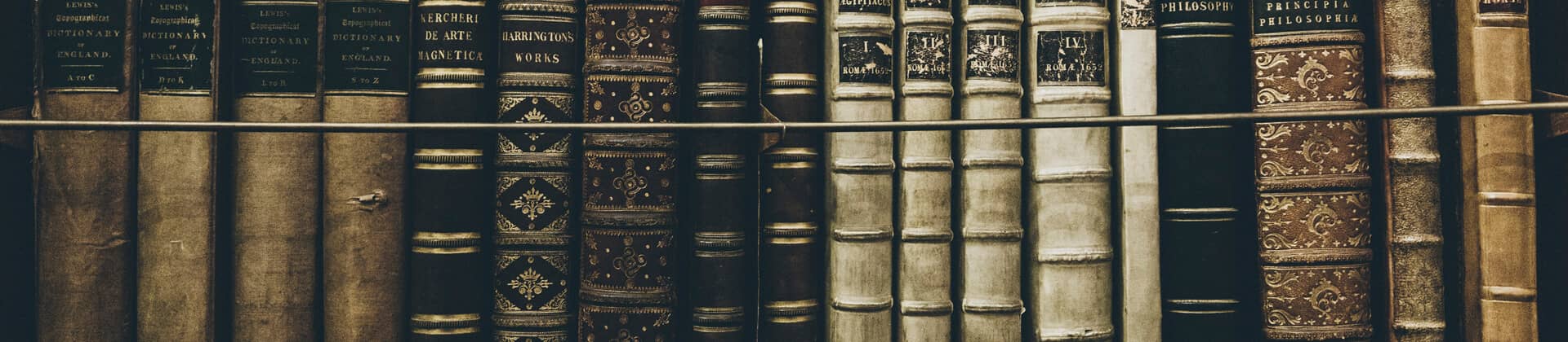 Close up of ornate, old books lined up on an unseen shelf for the Bachelor of Arts in Pre-Law Studies Program Pages