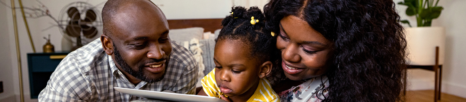 black man and woman with toddler girl between them smiling down at tablet